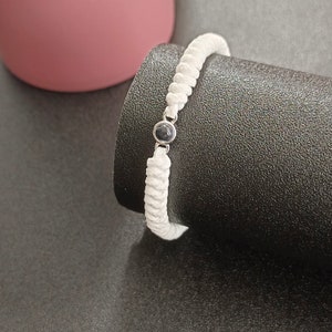 May include: White braided bracelet with a black bead accent.