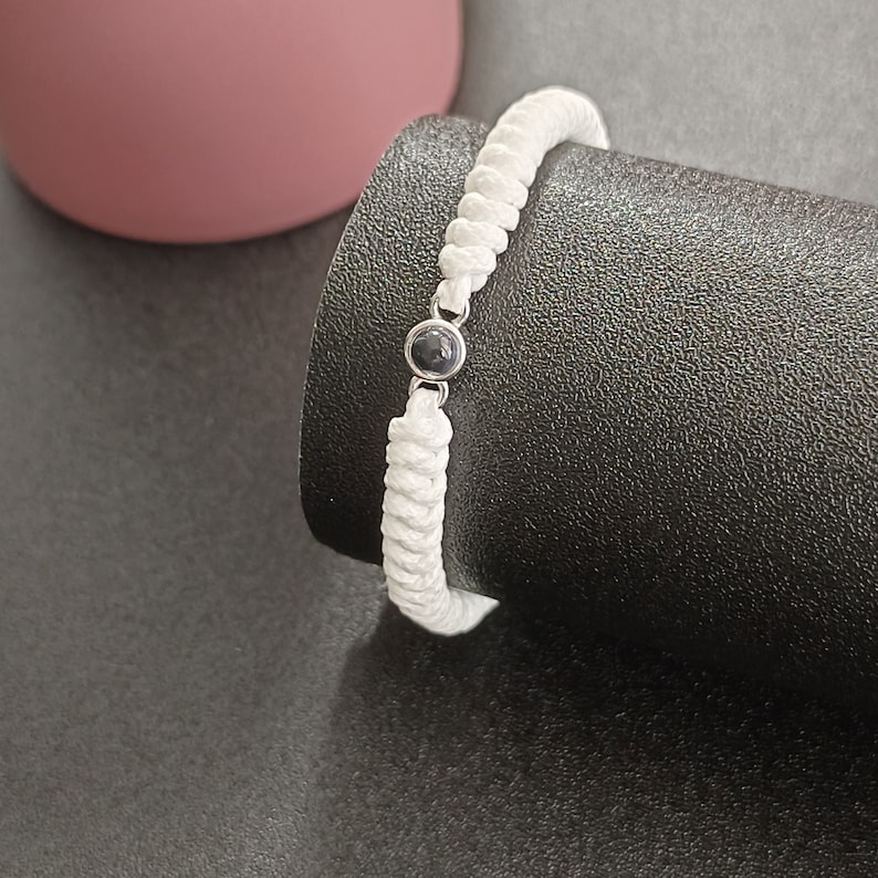 May include: White braided bracelet with a black bead accent.
