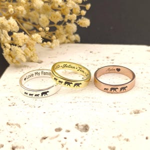 May include: Three rings in silver, gold, and rose gold. Each ring features a bear family design and personalised text. The silver ring says "Love My Family." The gold ring has names, and the rose gold ring has a name and a heart.
