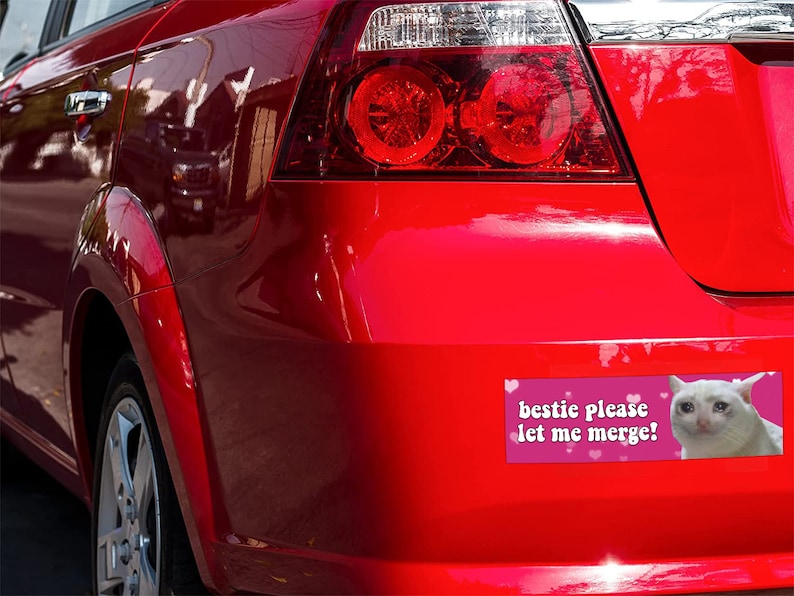 Peut inclure: Arri&egrave;re d'une voiture rouge avec un autocollant sur le pare-chocs. L'autocollant dit "bestie please let me merge!" et pr&eacute;sente un m&egrave;me d'un chat blanc en pleurs. Les feux arri&egrave;re de la voiture sont &eacute;galement visibles.