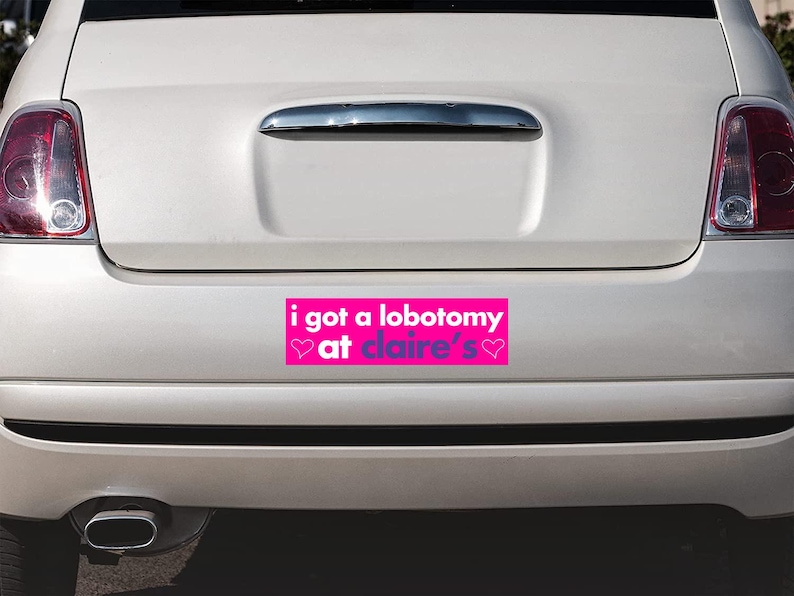 May include: A pink bumper sticker with the text "i got a lobotomy at claire's" in purple text with two pink hearts on either side of the text.