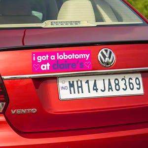 May include: A red car with a pink bumper sticker that reads "i got a lobotomy at claire's" with two pink hearts. The car has a license plate that reads "MH14JA8369".