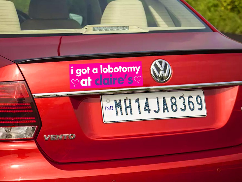 May include: A red car with a pink bumper sticker that reads "i got a lobotomy at claire's" with two pink hearts. The car has a license plate that reads "MH14JA8369".