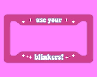 May include: Pink plastic license plate frame with the text "use your blinkers!" in white with a retro font and white stars on either side of the text.