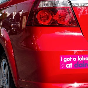 May include: A red car with a bumper sticker that reads "i got a lobotomy at claire's" with pink hearts on either side of the text.