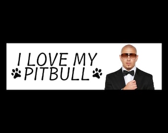 Puede incluir: Una pancarta blanca con texto negro que dice "I LOVE MY PITBULL" con una huella de pata negra a cada lado del texto. Un hombre con traje negro, pajarita negra y gafas de sol está en el fondo.