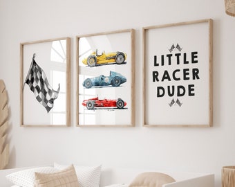 May include: Three framed prints on a white wall above a white daybed with a beige blanket. The prints feature a checkered flag, three vintage race cars, and the text "LITTLE RACER DUDE".
