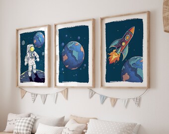 Pode incluir: Três impressões de arte emolduradas com tema espacial. Uma apresenta um astronauta, outra um planeta e a terceira um foguete. A obra de arte tem um fundo azul escuro com planetas e estrelas. As molduras são castanho claro, para um quarto infantil.