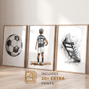 Peut inclure: Trois impressions encadrées sur le thème du football. L'une représente un ballon de football, une autre un garçon en uniforme de foot, et la troisième une chaussure de foot. Les impressions sont en noir, blanc et gris. Le texte "INCLUDES 20+ EXTRA PRINTS" est visible.