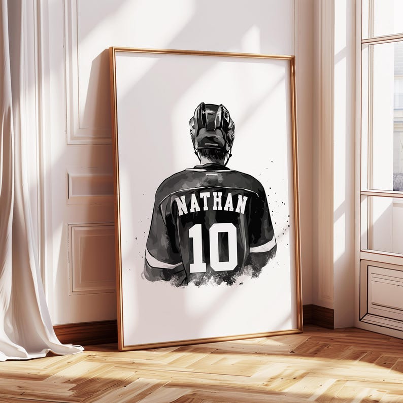May include: Framed art print featuring a hockey player from the back, wearing a black jersey with the name "NATHAN" and the number "10" in white. The player is wearing a black helmet. The artwork is in black and white.