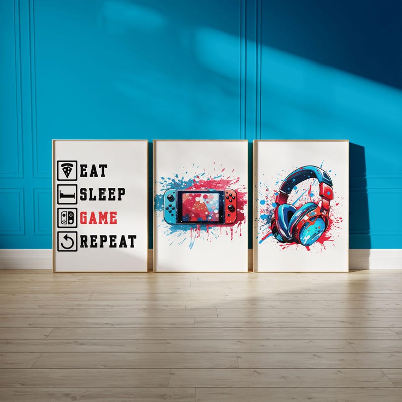 May include: Three framed art prints with a gaming theme. One print reads "EAT SLEEP GAME REPEAT". The other two prints feature a game controller and headphones, with red and blue paint splatter designs. The frames are gold.