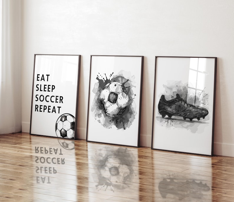May include: Three framed black and white soccer-themed art prints. One print reads "EAT SLEEP SOCCER REPEAT" with a soccer ball illustration. The other two prints feature soccer ball and cleat illustrations with watercolor-style splatters.