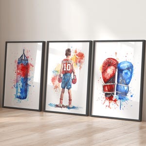 May include: Three watercolor paintings on canvas with black frames. The first painting shows a red and blue boxing bag with watercolors splattered around it. The second painting shows a young boxer wearing red shorts and a red and white jersey with the number 10 on it. The third painting shows a pair of boxing gloves, one red and one blue, with watercolors splattered around them.