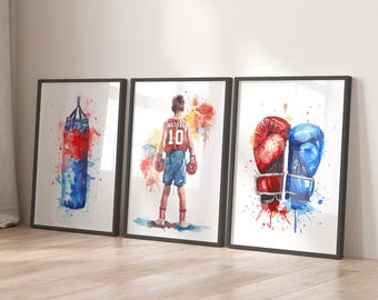 May include: Three watercolor paintings on canvas with black frames. The first painting shows a red and blue boxing bag with watercolors splattered around it. The second painting shows a young boxer wearing red shorts and a red and white jersey with the number 10 on it. The third painting shows a pair of boxing gloves, one red and one blue, with watercolors splattered around them.
