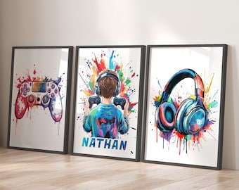May include: Three framed wall art prints featuring vibrant watercolor-style splashes. The left print shows a game controller, the center print depicts a person wearing headphones and holding a controller with the name NATHAN, and the right print displays a pair of headphones.