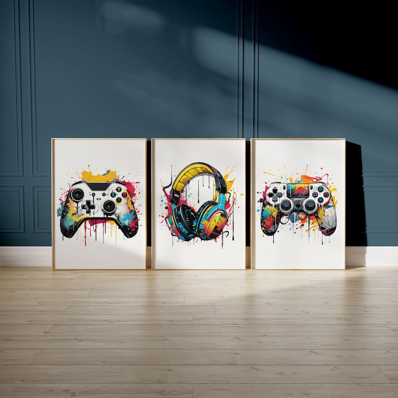 May include: Three framed art prints featuring colorful watercolor designs. The prints depict a video game controller, headphones, and another controller. Each image has a white background and a gold frame, with paint splatter effects.
