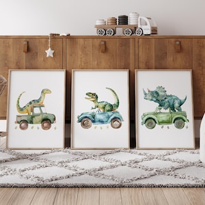 Pode incluir: Tr&ecirc;s impress&otilde;es de aquarela com dinossauros dirigindo carros. As impress&otilde;es s&atilde;o emolduradas em madeira clara e s&atilde;o exibidas em uma prateleira de madeira. Os dinossauros s&atilde;o um tricer&aacute;topo verde, um estegossauro verde e um tiranossauro rex verde.