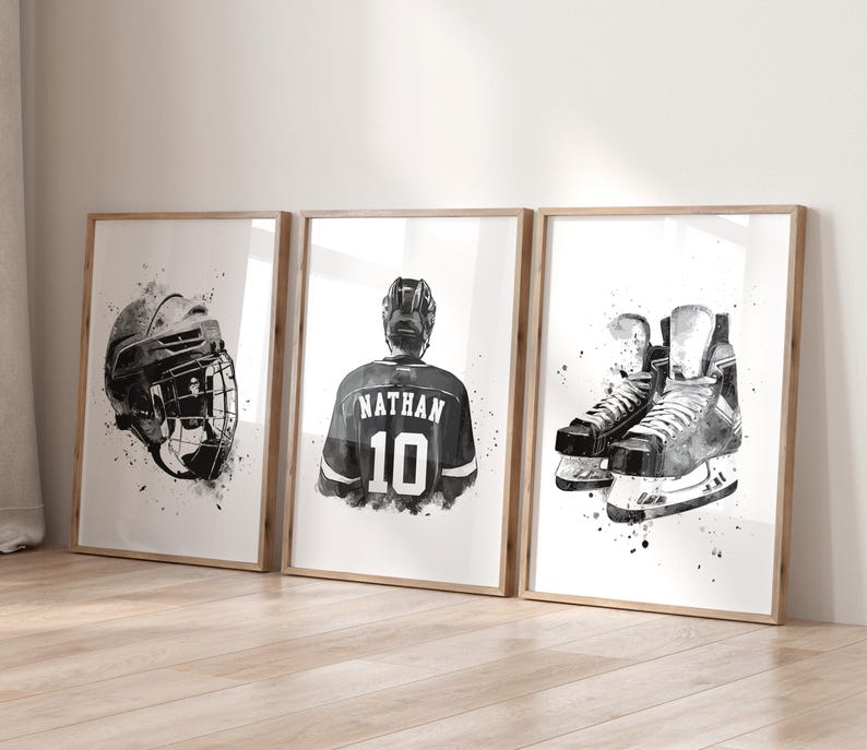 May include: Three framed black and white watercolor prints featuring hockey equipment. The prints depict a hockey helmet, a jersey with "NATHAN 10" on the back, and a pair of ice skates. The artwork has a splattered paint effect.