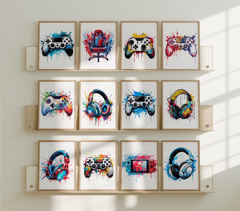 May include: A collection of framed art prints featuring watercolor illustrations of gaming accessories. The prints include game controllers, gaming headsets, and a gaming chair, all with colorful splatter backgrounds. The artwork is displayed on wooden shelves.