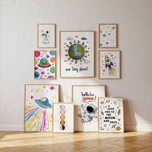 May include: A collection of framed art prints with a space theme. The prints feature colorful illustrations of planets, rockets, a UFO, and an astronaut. Some prints include text such as "Our Tiny Planet" and "Hello from space!"