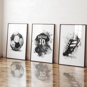May include: Three framed black and white watercolor prints featuring soccer-themed art. The prints depict a soccer ball, a jersey with the name "Nathan" and the number 10, and a soccer cleat.
