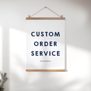 以下が含まれることがあります： 木製のフレームに吊るされた、紺色の「CUSTOM ORDER SERVICE」という文字が書かれた白いポスター。「DECORBYREECE」の文字が下にあります。ポスターは茶色のコードで吊るされています。