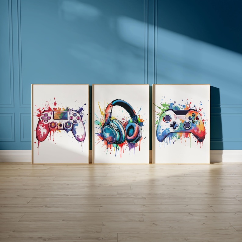 May include: Three framed art prints featuring watercolor illustrations of gaming accessories. The prints depict a red and purple controller, blue headphones, and a multicolored controller, all with colorful paint splatter backgrounds.