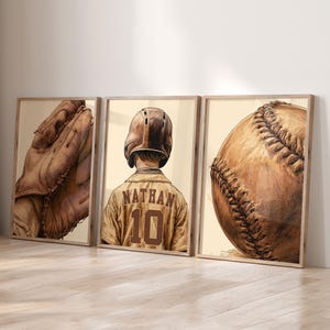 May include: A set of three framed wall art prints featuring baseball themes. The left print shows a leather baseball glove, the center print depicts a baseball player wearing a helmet and jersey with the name NATHAN and number 10, and the right print shows a baseball.
