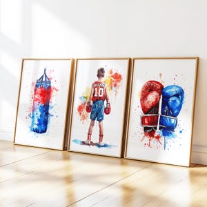 May include: Three watercolor paintings in gold frames depicting boxing imagery. The first painting shows a blue and red boxing bag. The second painting shows a boxer wearing red shorts and a red and white jersey with the number 10 on it. The third painting shows a pair of boxing gloves, one red and one blue.