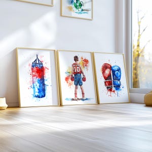 May include: Three watercolor paintings on canvas with gold frames. The first painting shows a red and blue boxing bag with watercolors splattered around it. The second painting shows a boxer in a red and white uniform with the number 10 on the back. The third painting shows a pair of red and blue boxing gloves with watercolors splattered around them.