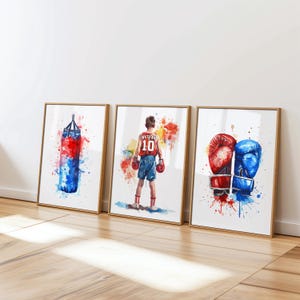 May include: Three framed watercolor paintings depicting boxing imagery. The first painting shows a red and blue boxing bag. The second painting shows a boxer wearing red shorts and a red and white jersey with the number 10 on it. The third painting shows a pair of boxing gloves, one red and one blue.