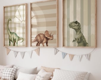 May include: Three framed wall art prints featuring watercolor illustrations of a green long-necked dinosaur, a brown triceratops, and a green tyrannosaurus rex, each set against a neutral-toned background with stripes or checkered patterns.