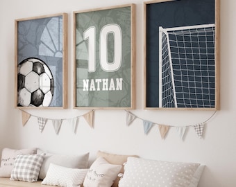 May include: Three framed wall art prints featuring a soccer theme. The left print shows a soccer ball, the center print displays the number 10 and the name NATHAN, and the right print depicts a soccer goal net against a dark blue background.