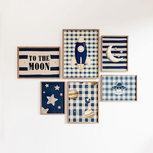May include: A set of six framed wall art pieces with a space theme. The art features a rocket, moon, stars, planets, and a UFO, all in a blue and beige color scheme. One piece has the text "TO THE MOON".