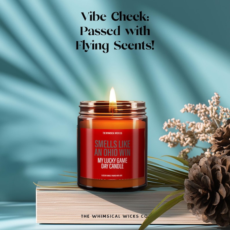 “Smells Like an Ohio Win” candle surrounded by flowers and decor, styled for game day vibes. Light humor and sporty charm make it a unique gift. Amber jar glows warmly. Ideal for tailgate lovers and fanatics alike. 100% soy wax, hand-poured with love.