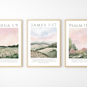 May include: A triptych of framed art prints with watercolour landscapes and Bible verses. Each print is in a light wood frame and features text from Joshua 1:9, James 1:17, and Psalm 139:14. The art shows fields and trees.