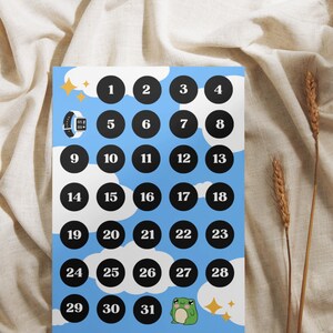 May include: A blue and white printable calendar with black circles numbered 1 through 31. The calendar features a cartoon frog and stars.