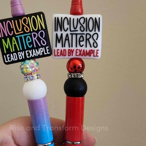 May include: Two pens with colorful ombre designs and black and white signs that read "Inclusion Matters Lead by Example".