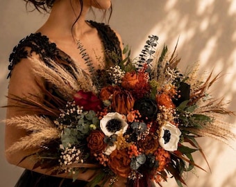 May include: A large, rustic bouquet featuring a variety of dried flowers and foliage. The arrangement includes pampas grass, anemones, and roses in shades of orange, red, and cream, with accents of green and black. The bouquet is tied with a burgundy ribbon.