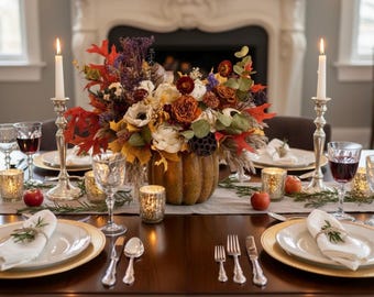 May include: A beautifully set dining table with a fall theme. A large pumpkin-shaped vase holds a floral arrangement. Candles, wine glasses, and place settings with gold-rimmed plates complete the elegant autumn scene. The table is set for a special occasion.