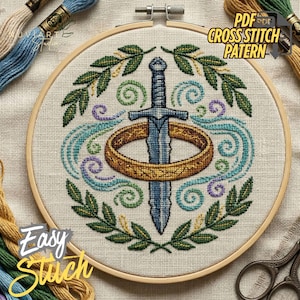 Könnte beinhalten: Kreuzstichmuster mit einem blauen Schwert, das einen goldenen Ring durchbohrt, umgeben von grünen Blättern und wirbelnden blauen und lila Akzenten. Das Design befindet sich in einem hölzernen Stickrahmen. Text: "PDF Cross Stitch Pattern" und "Easy Stitch".
