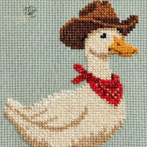 K&ouml;nnte beinhalten: Kreuzstichbild einer Gans mit braunem Cowboyhut und rotem Halstuch. Die Gans hat einen gelben Schnabel und ist vor einem hellblauen Hintergrund platziert. Der Kreuzstich ist detailliert und strukturiert.