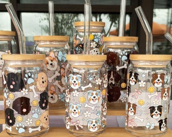 May include: Six glass tumblers with cork lids and straws. Each tumbler features a different cartoon dog design. The tumblers are arranged on a wooden shelf with two cork flower-shaped coasters in the foreground.