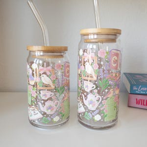 May include: Two clear glass drinking cups with bamboo lids and glass straws. The cups feature a floral design with teacups, teapots, birds, and the text "People of Peace". The design includes pink, purple, and green elements.
