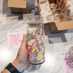 May include: A clear glass tumbler with a bamboo lid and a straw. The tumbler is decorated with a whimsical floral and owl design. The words "today is going to be an Amazing day!" are on a pink guest check.
