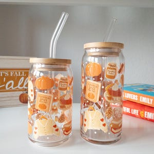 May include: Two clear glass tumblers with bamboo lids and glass straws. The tumblers are decorated with fall-themed illustrations, including pumpkins, sweaters, and the text "Pumpkin Spice Recipes".