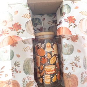 May include: A glass tumbler with a bamboo lid and straw, decorated with fall-themed illustrations, including pumpkins, leaves, and candles. The tumbler is inside a cardboard box lined with pumpkin-printed paper. The words "Pumpkin Butter" are visible on the tumbler.