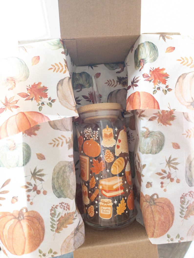May include: A glass tumbler with a bamboo lid and straw, decorated with fall-themed illustrations, including pumpkins, leaves, and candles. The tumbler is inside a cardboard box lined with pumpkin-printed paper. The words "Pumpkin Butter" are visible on the tumbler.