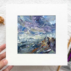 Puede incluir: Pintura al óleo original de un paisaje con un estilo impasto texturizado. La obra presenta una paleta de azules, morados y naranjas, montada en un passe-partout blanco. Se ven un pincel y un tubo de pintura morada.