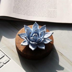 May include: A light blue ceramic flower with a wooden base. The flower is in the shape of a lotus and has a delicate, intricate design.